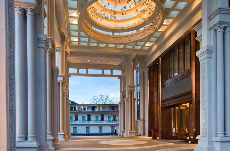 Grand hotel entrance with tall stone columns, ornate ceiling chandelier, and modern glass doors.