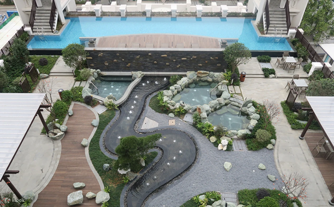 Outdoor spa area with hot spring pools, landscaped garden, wooden walkways, and a large swimming pool.