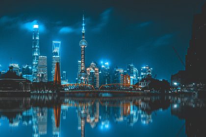 Shanghai skyline at night with Oriental Pearl Tower, modern skyscrapers, and reflections on the river.