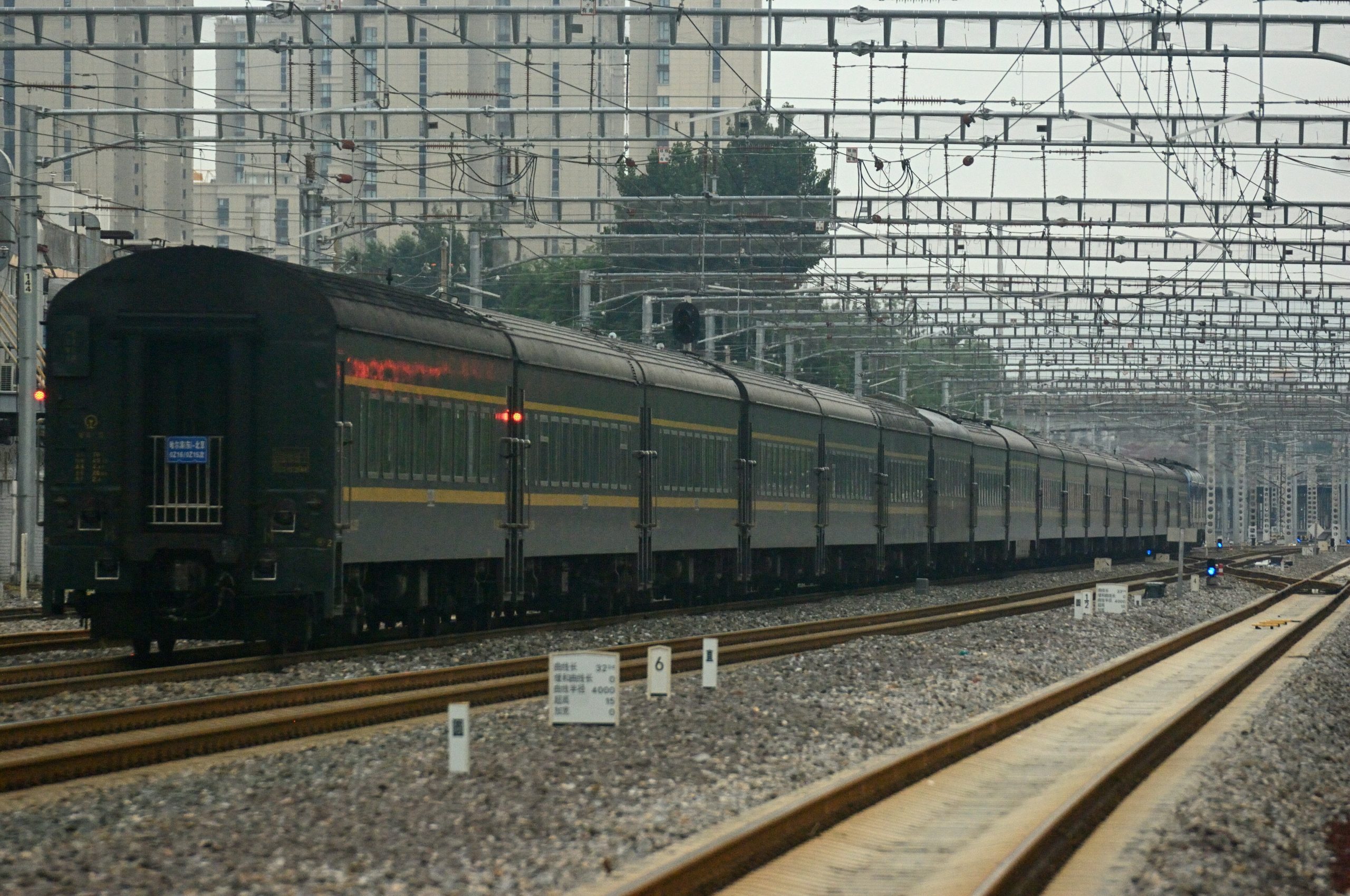 Long green passenger train with yellow stripe traveling on railway tracks under overhead wires
