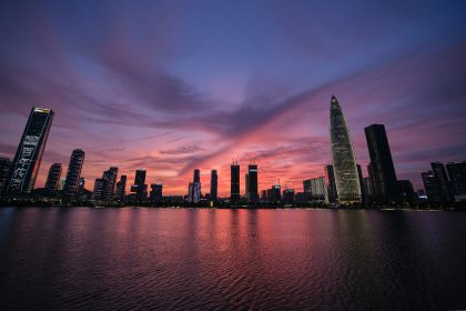 : Shenzhen city skyline at sunset with illuminated skyscrapers reflected in waterfront