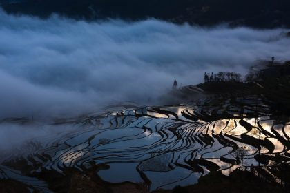 Terraced Hani rice fields reflecting light under low clouds and misty mountain landscape.