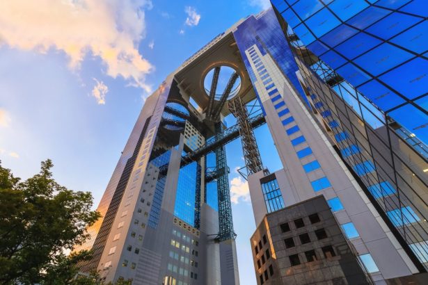 Low-angle view of the Umeda Sky Building in Osaka, Japan, showing its twin towers connected by a circular observatory against a blue sky.