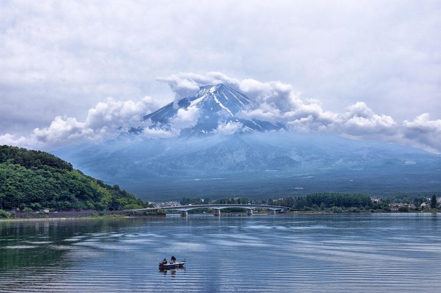 Mount Fuji rising above a calm lake, bridge and small fishing boat in foreground