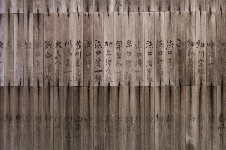 Traditional Japanese calligraphy written on vertical wooden planks, showcasing weathered wood and dark ink brush strokes.