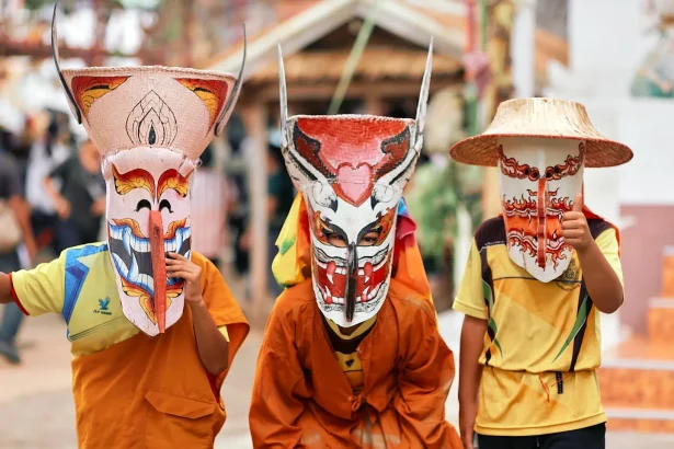 Three children wearing colorful Phi Ta Khon masks and traditional clothing during a festival in Thailand.
