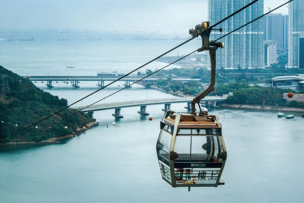 Cable car traveling over water near bridges and high-rise buildings on route to Lantau Island hiking trails.