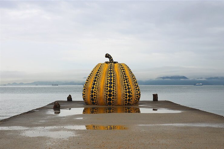 Image by Japan-Guide.com Setouchi Triennale yellow pumpkin sculpture with black dots on pier by the sea