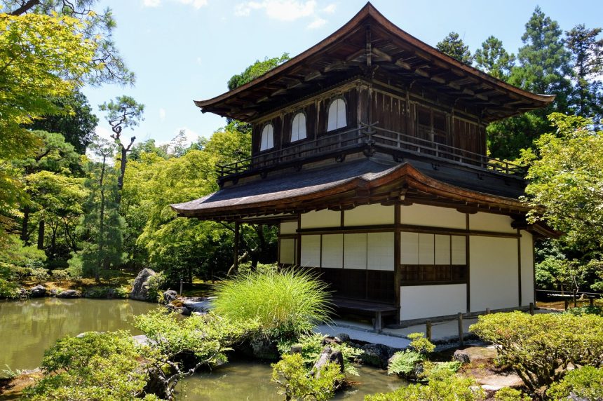 Traditional wooden pavilion surrounded by lush green trees and pond in Kyoto during summer.