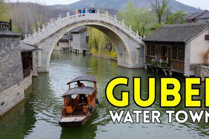 Wooden boat under stone arch bridge in Gubei Water Town with traditional houses and hills.