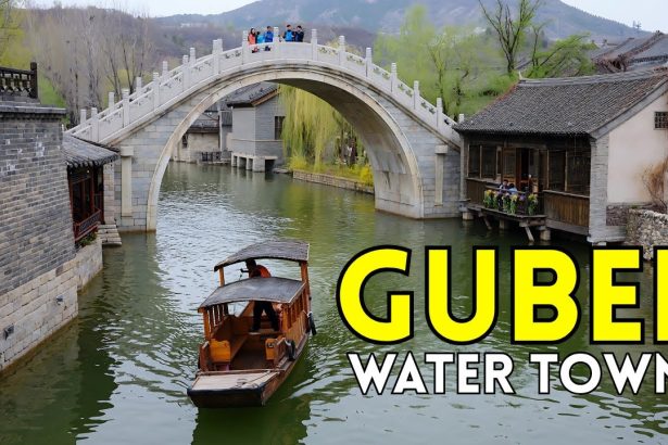 Wooden boat under stone arch bridge in Gubei Water Town with traditional houses and hills.
