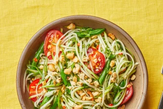 Thai green papaya salad with tomatoes, peanuts, chili, and green beans in a ceramic bowl. Title: Thai Green Papaya Salad