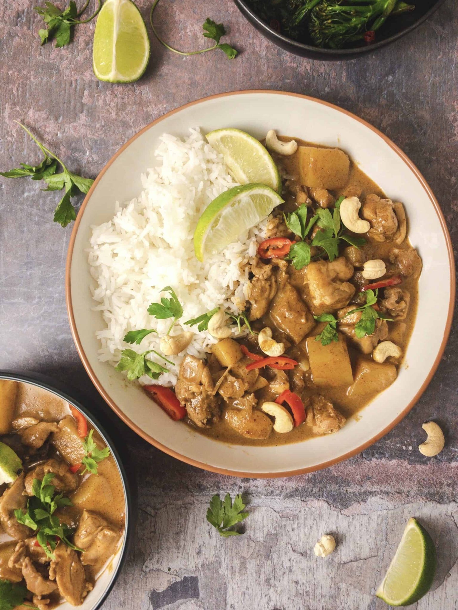Thai massaman curry with chicken, potatoes, cashews, and white rice garnished with lime and herbs.
