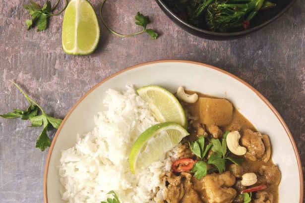 Thai massaman curry with chicken, potatoes, cashews, and white rice garnished with lime and herbs.