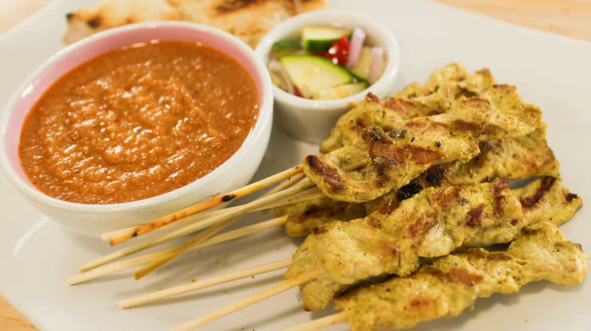 Grilled chicken satay skewers with peanut sauce and cucumber relish on plate