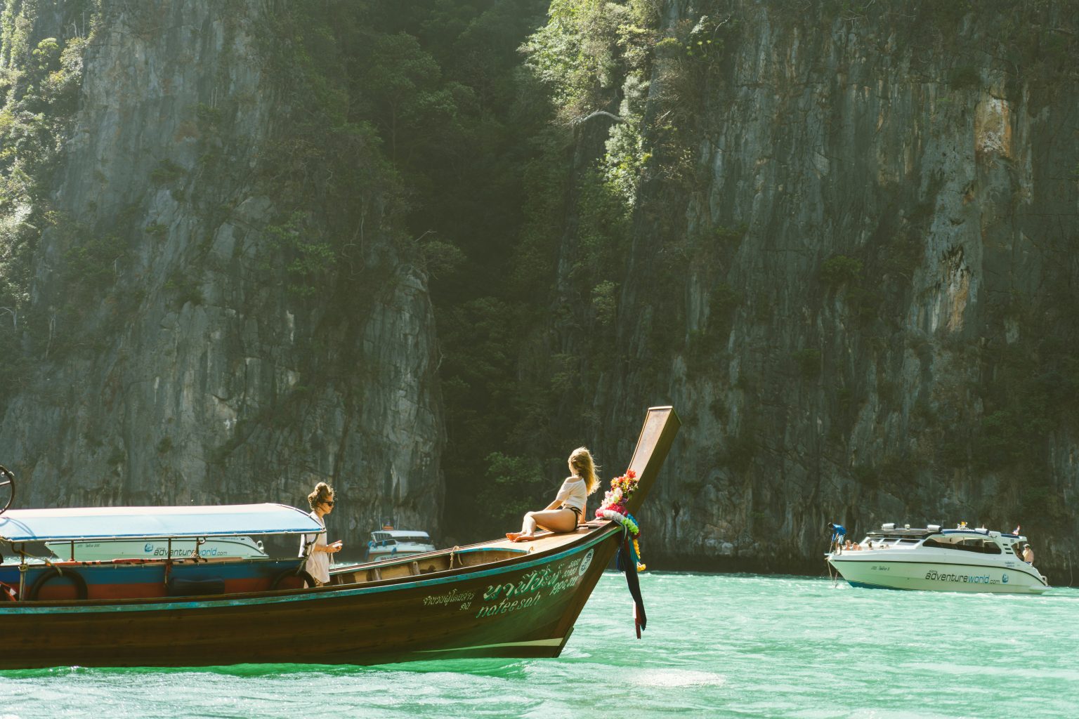 Traditional wooden boat sailing on the calm turquoise waters of the Andaman Sea near Thailand’s limestone cliffs and tropical islands.
