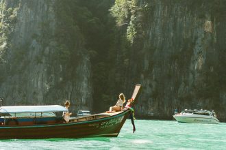 Traditional wooden boat sailing on the calm turquoise waters of the Andaman Sea near Thailand’s limestone cliffs and tropical islands.