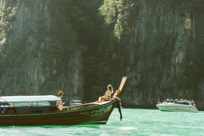 Traditional wooden boat sailing on the calm turquoise waters of the Andaman Sea near Thailand’s limestone cliffs and tropical islands.