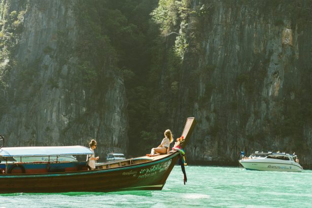 Traditional wooden boat sailing on the calm turquoise waters of the Andaman Sea near Thailand’s limestone cliffs and tropical islands.