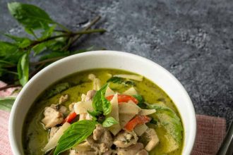 Thai green curry with chicken, bamboo shoots, red peppers, and fresh basil in white bowl