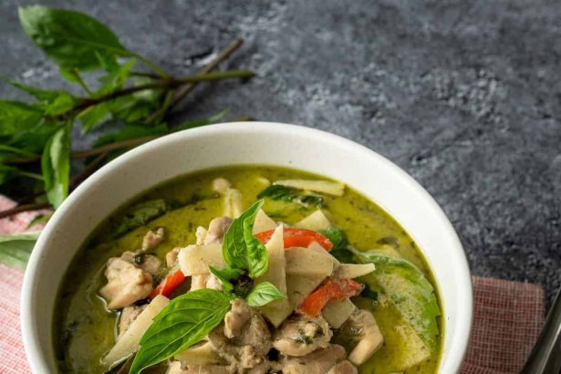 Thai green curry with chicken, bamboo shoots, red peppers, and fresh basil in white bowl