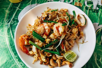 Plate of seafood Pad Thai topped with shrimp, squid, tofu, bean sprouts, green onions, and roasted cashews, garnished with a lime wedge.