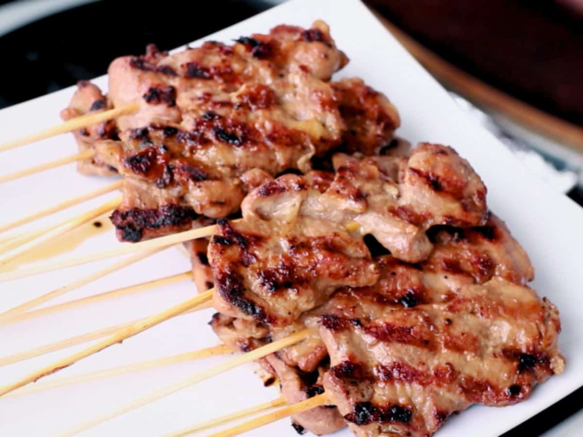 Grilled Moo Ping pork skewers with charred marks served on a white plate, a popular Thai street food.