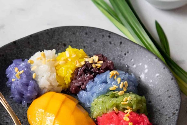 Plate of Thai mango sticky rice with colorful glutinous rice in six colors topped with sesame seeds
