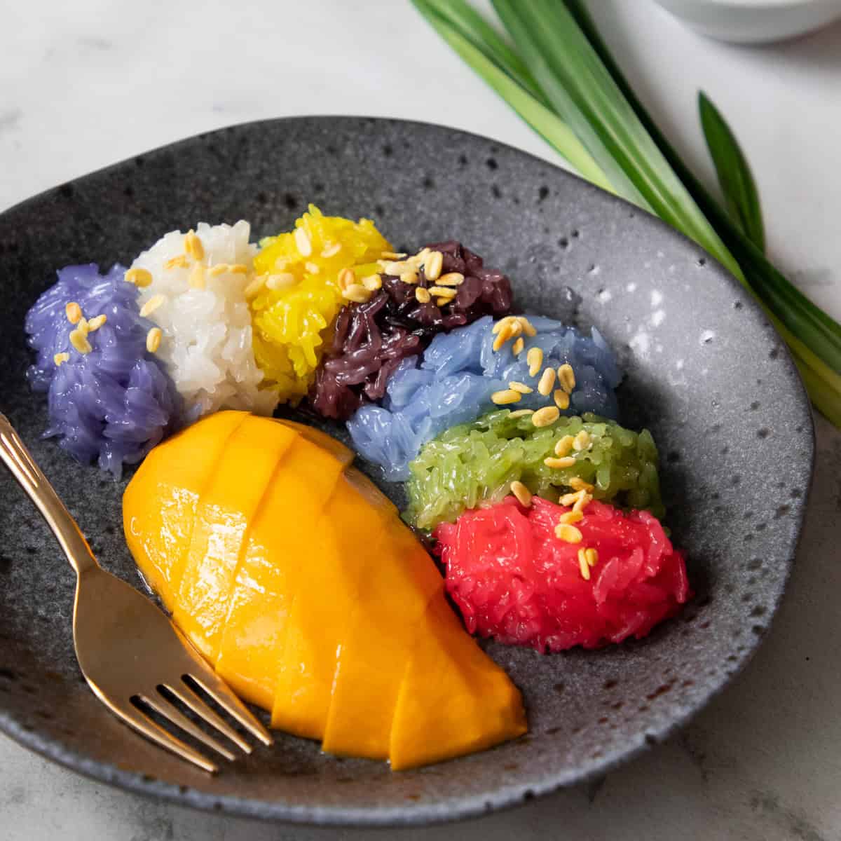 Plate of Thai mango sticky rice with colorful glutinous rice in six colors topped with sesame seeds
