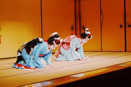 Two traditionally dressed Japanese Maiko performers gracefully bow on a tatami stage, showcasing cultural etiquette and elegance in Kyoto, Japan.