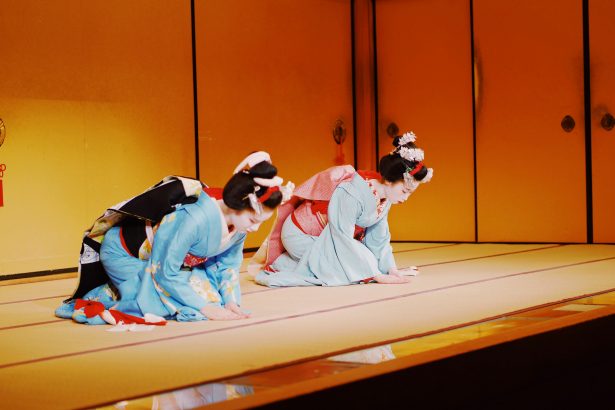 Two traditionally dressed Japanese Maiko performers gracefully bow on a tatami stage, showcasing cultural etiquette and elegance in Kyoto, Japan.